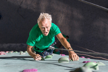 Aged Person Practicing Extreme Sport Elderly Male Climber Makes Hard Move on Outdoor Climbing Wall Sporty Clothing on Fitness Training Course Intense but Positive Face Using Rope and Belaying Gear