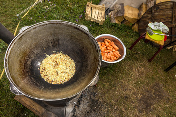 Cooking in Vintage Large Pan Large Old Fashioned Iron Kettle and Onion Grilling Bowl with Carrot and other Ingredients and Kitchen Utensils on Background 