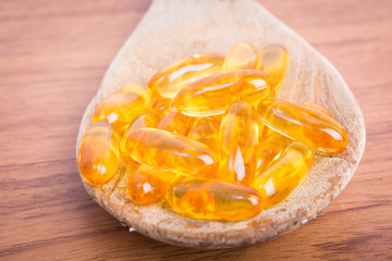 Cod liver oil omega 3 gel capsules on spoon wood