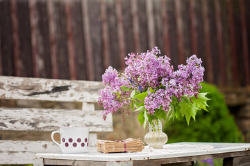Lilac in a vase on a table, book and coffee mug next to him