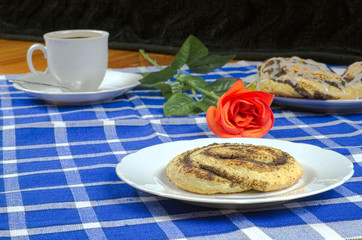 Homemade cake with poppy seeds in the shape of a snail with a cup of coffee, red rose