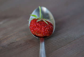 ripe strawberry in a spoon on wooden background