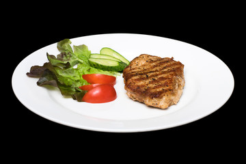 Photo of a pork stake on a white plate with a cucumber, tomato a
