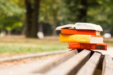 Stack of hardback book and Open book lying on a bench at park on blurred nature backdrop. Copy space, back to school. Education background.