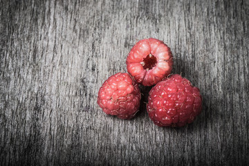 Three fresh raspberry on the old gray wooden board. Toned