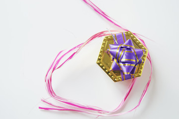 Nice golden gift box with a violet bow and decorative ribbon around pink colour, all isolated on white background. Left copyspace.