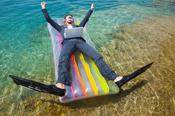 Happy businesswoman in goggles and flippers with laptop on floating mattress. Travel concept 