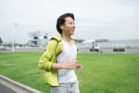 Happy Young Asian Man Running In City Park