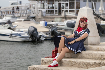 View of pinup young woman in vintage style clothing on a marina.