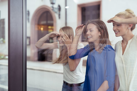 drei freundinnen schauen durch das schaufenster in ein geschäft