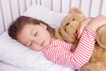 cute little girl sleeping with stuffed toy in her bed
