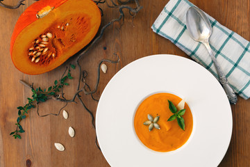 Pumpkin soup, seeds, bread and basil in plate on wood background
