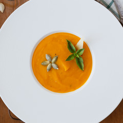 Pumpkin soup, seeds, bread and basil in plate on wood background