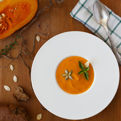 Pumpkin soup, seeds, bread and basil in plate on wood background