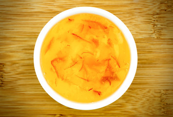 Orange marmalade jam in a white bowl against a wooden table