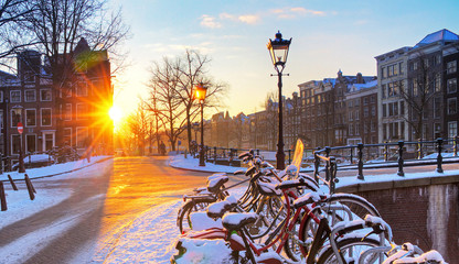 Sunrise over the canal streets of Amsterdam, the Netherlands, with bicycles covered in snow on a...