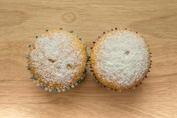 Two homemade cupcakes with powdered sugar on wooden board