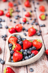 strawberries , raspberries, blueberries in a bowl on a wooden background
