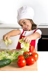 happy little girl playing with vegetables at home kitchen in apron and cook hat