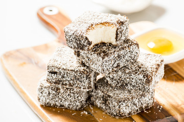 Group of Lamingtons on a timber cutting board with food ingredients in the background 