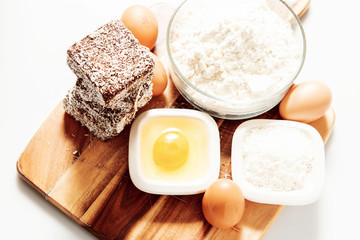 Group of Lamingtons on a timber cutting board with food ingredients in the background 
