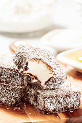 Group of Lamingtons on a timber cutting board with food ingredients in the background 