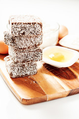 Group of Lamingtons on a timber cutting board with food ingredients in the background 