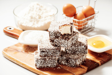Group of Lamingtons on a timber cutting board with food ingredients in the background 
