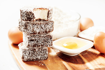 Group of Lamingtons on a timber cutting board with food ingredients in the background 