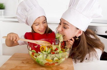 happy mother and little daughter at home kitchen preparing salad in apron and cook hat