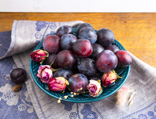 Purple plums in a green plate on a wooden table