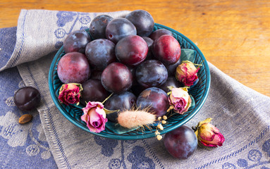 Purple plums in a green plate on a wooden table