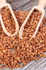 Heap of buckwheat groats with spoon on wooden surface