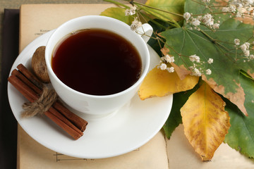 Cup of tea with cinnamon and a book with dried flowers and walnut on wooden background