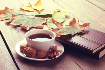 Naklejka na ściany i meble Cup of tea with cinnamon and a book and walnut on wooden background,filter