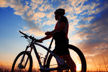 Silhouette of a biker and bicycle on sunset background.