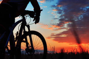 Naklejka na ściany i meble Silhouette of a biker and bicycle on sunset background.