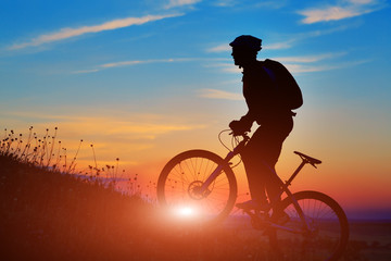 Naklejka na ściany i meble Silhouette of a biker and bicycle on sunset background.