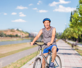 Naklejka premium Cheerful senior posing with his bike on a sidewalk