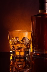 glass of whiskey near bottle on black table with reflection, warm tint atmosphere