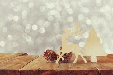 abstract image of wooden decorative christmas tree, reindeer and pine cones on wooden table and christmas holiday bokeh lights and snowflakes overlay
