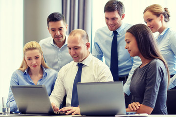 smiling businesspeople with laptops in office