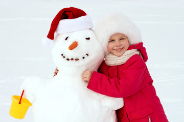 little girl hugging a snowman and laughs. Winter fun