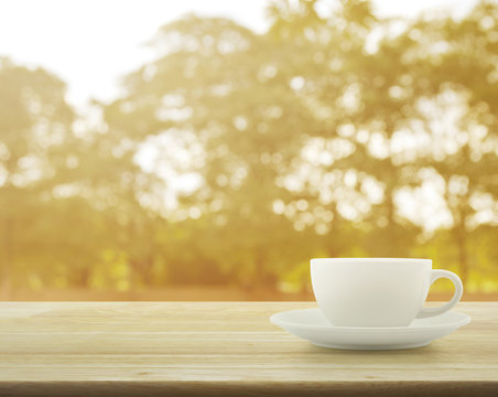 White cup on wooden table over tree bokeh background