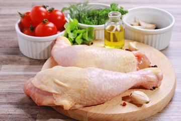 Raw chicken legs decorated with salad, olive oil and cherry tomatoes on white plate. Diet food, healthy lifestyle