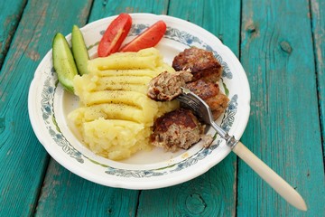 Mashed potatoes and three homemade meat chops with fresh cucumbe
