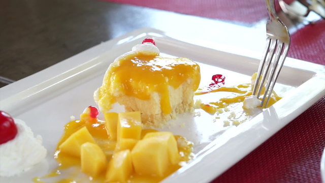Eating Mango Cheese Cake on white plate with fresh fruit decoration