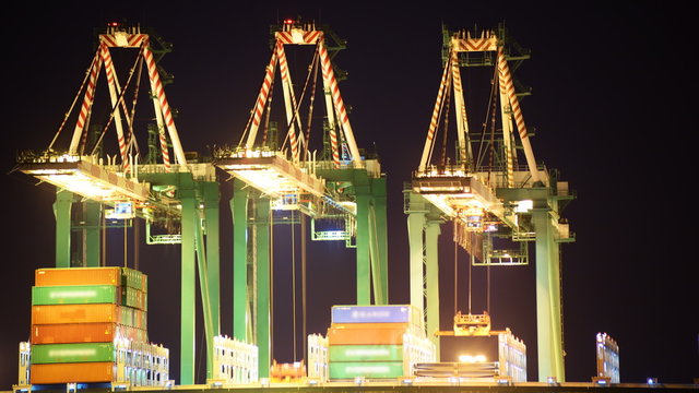 Time lapse footage with zoom in motion of industrial cranes loading containers onto container ship at a shipyard in port of Los Angeles at night