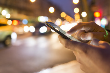 Man using his Mobile Phone in the street, night light bokeh Background