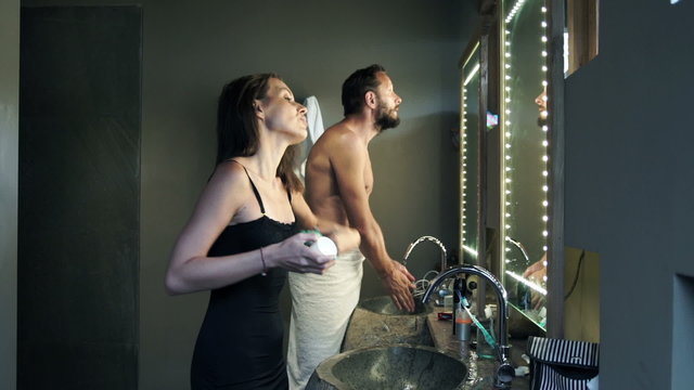 Couple in bathroom, man washing hands and woman applying antiperspirant
